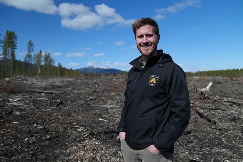 A man stands in a clearcut area on a sunny day.