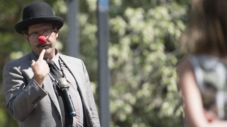 A man wears a clown nose in an outdoor setting.