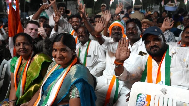 People sit for a rally. They hold their hands up.