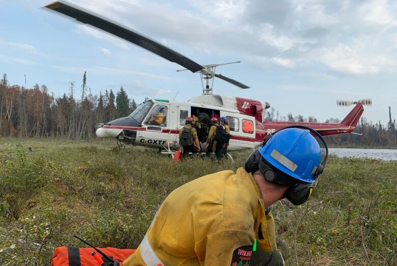 Firefighters gather near a helicopter in a forest clearing.