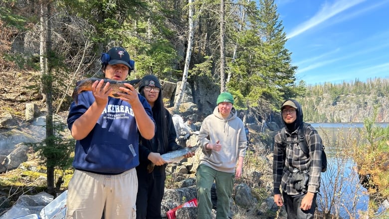 Four high school students stand close to the shore and two of the students are holding up a fish.