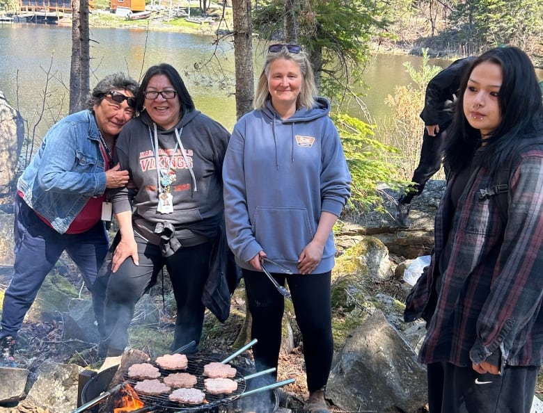 teacher and support workers stand in front of a fire pit as they grill hamburgers and fish for their shore lunch and lesson.