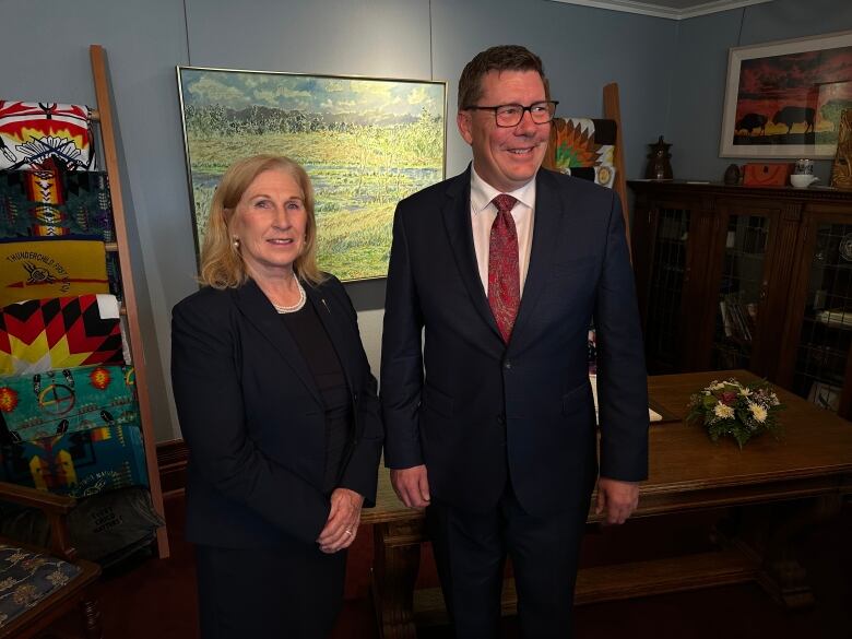 A woman and a man, both wearing dark, formal clothing, pose for a photo. 