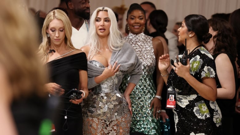 Several women in dresses stand in a crowd.