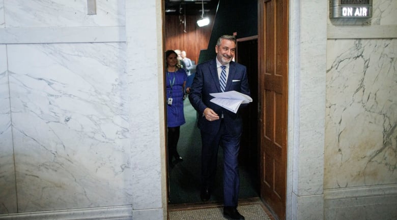 Paul Calandra steps through a doorway next to a lighted sign saying 'On Air.' 