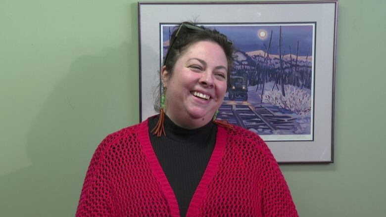 A woman wearing a read cardigan smiles widely 