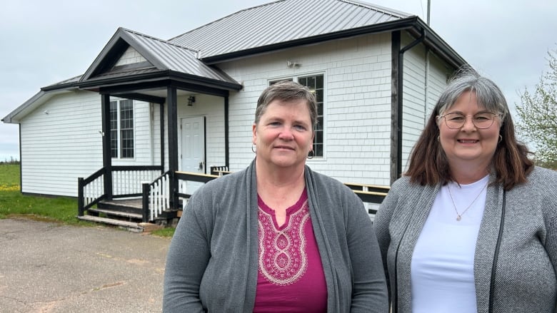 Two women standing in front of white building.