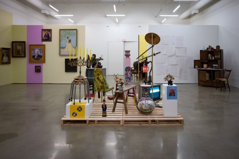 In a museum with white walls, four wood packing pallets create the stage for a collection of movie props, including a TV, bench, candelabra and vase