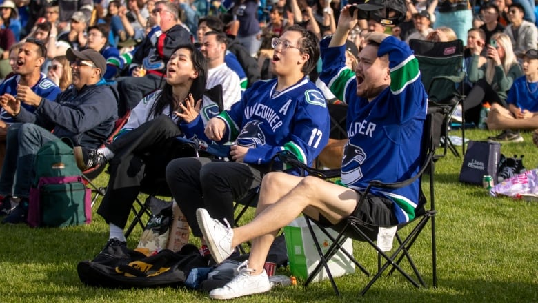 Fans wearing blue gesture in surprise and shock at a large outdoor event in a park.