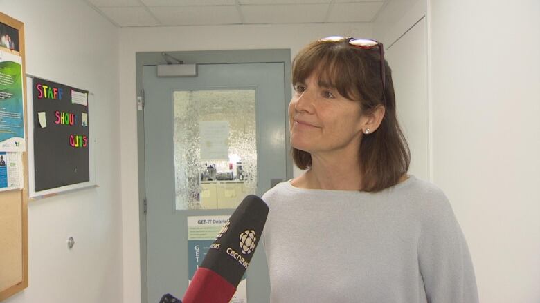 A woman in grey standing in front of a microphone