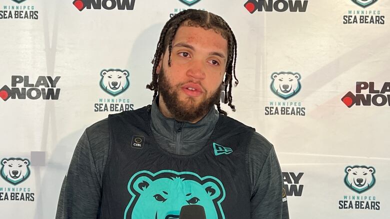 A man with braided hair wears a basketball jersey with a polar bear image