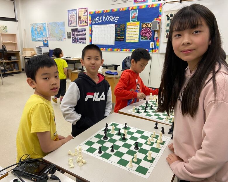 A group of kids gathers around a fabric chess board.