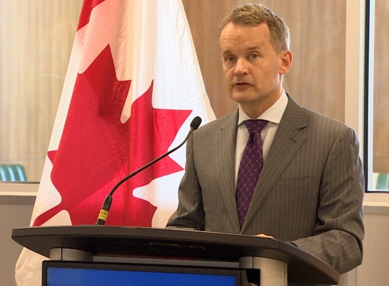 Man stands at a podium with a Canadian flag behind him