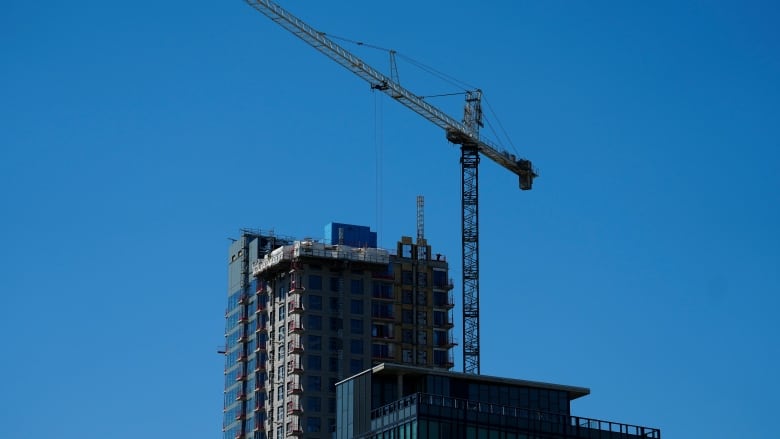 A highrise building under construction against a blue sky. There's a crane next to the building.