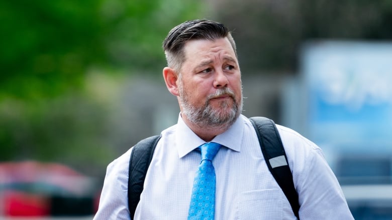 A man in a blue tie and light dress shirt outside on a sunny spring day.