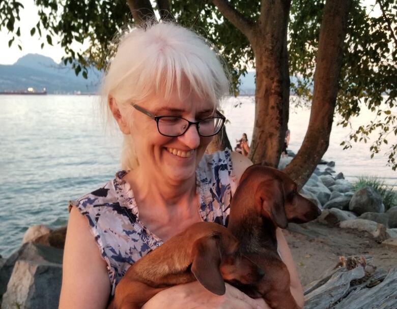 A senior-age woman carries a small dog.