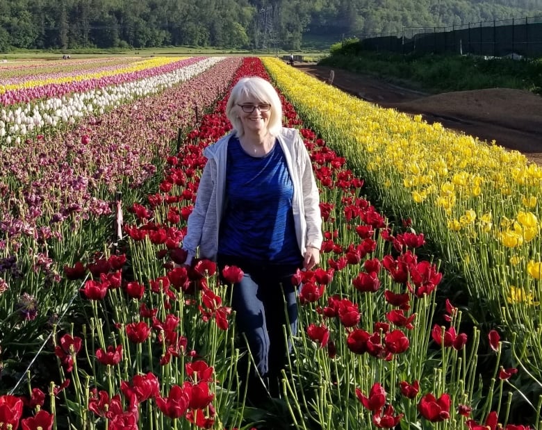 A senior-age woman stands in a field of tulips.