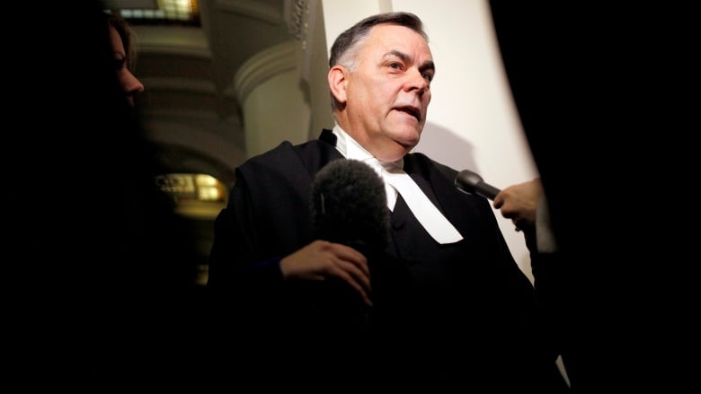 A white man wearing a speaker's uniform speaks to reporters.