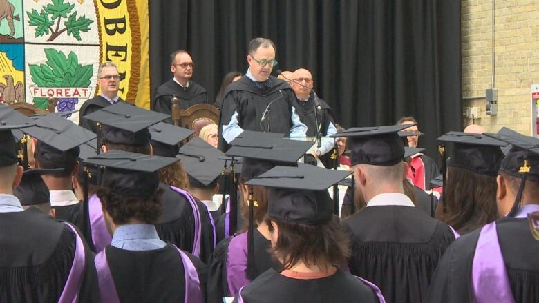 A man is pictured speaking at a podium to a group of graduates.