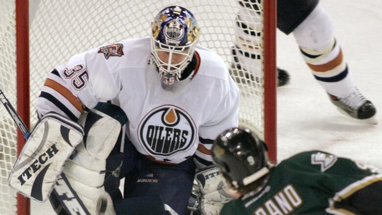 A goalie in an oilers jersey kneels in net. 