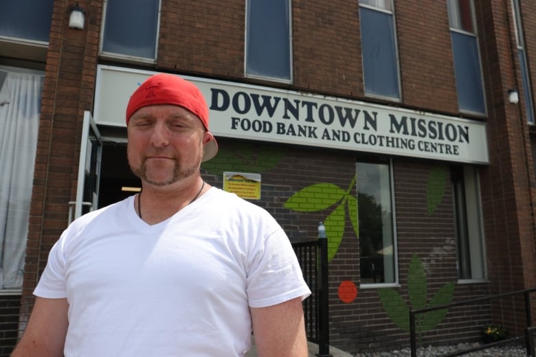 A man stands in front of a sign that reads, Downtown Mission.