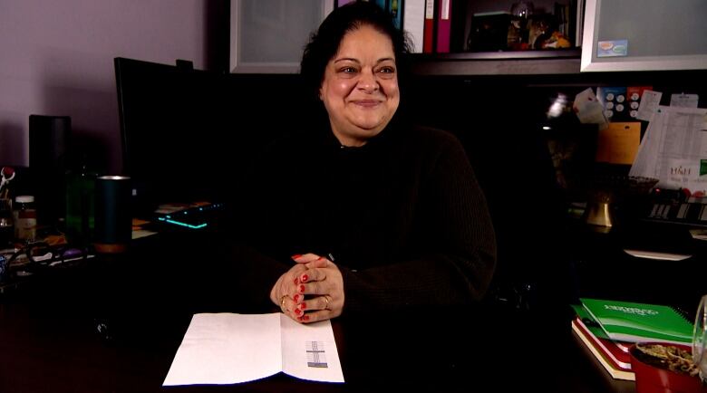 Bindu Narula is sitting at her desk with her hands clasped together, resting on a piece of  paper. 