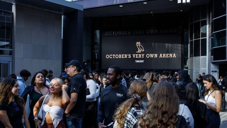 A crowd of people outside an arena, before a concert.