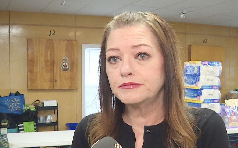 A woman with long light-brown hair speaks into a reporter's microphone.