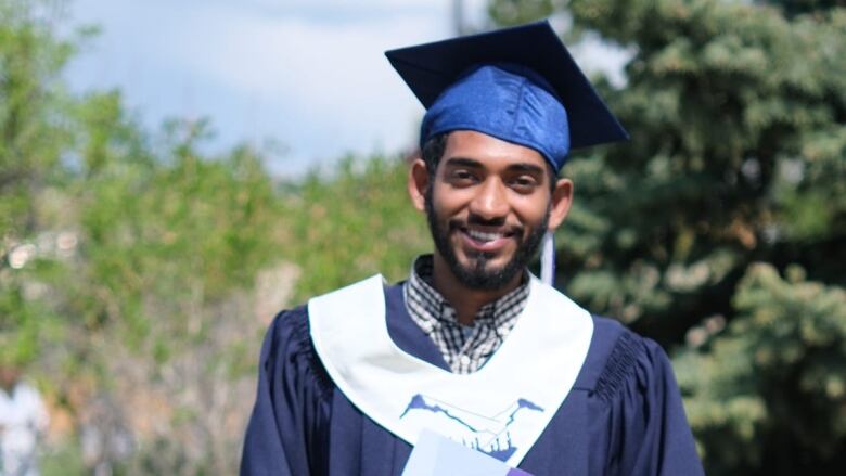 A man stands in a cap and gown, holding a diploma.