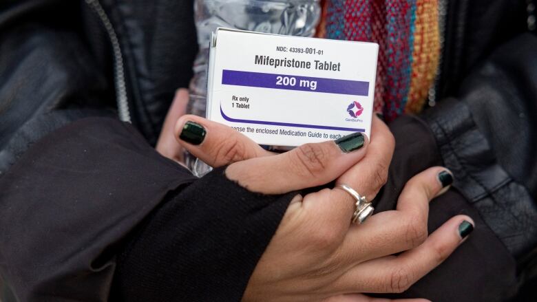 A person's hand is shown holding a small box of medication, called mifepristone.