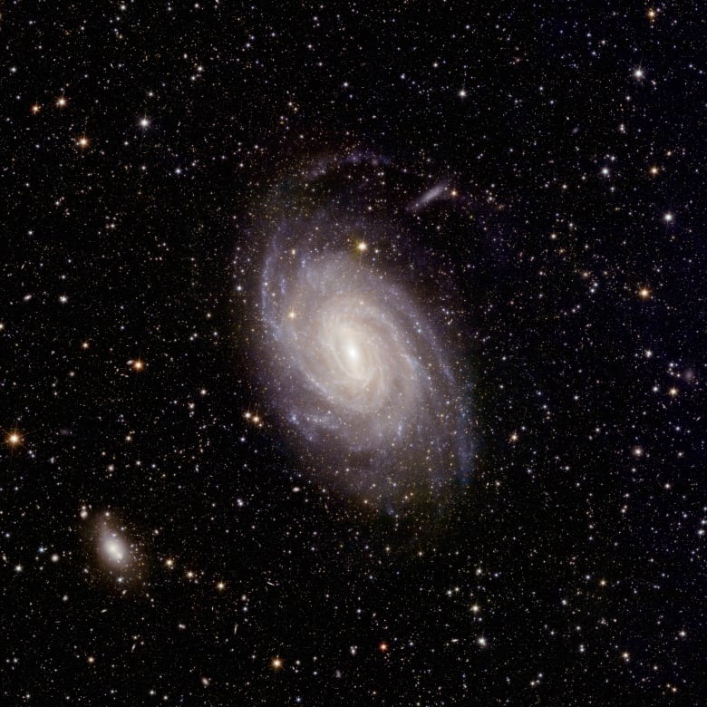 A spiral galaxy sits among thousands of other points of light, which include stars and galaxies.