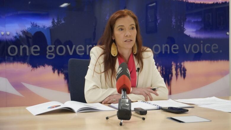 Woman in blazer sits at microphone.