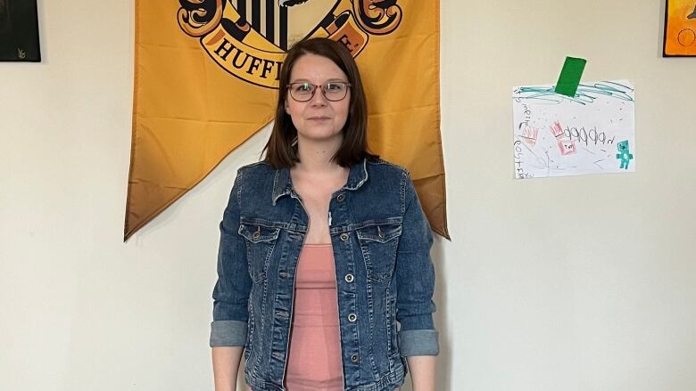 A woman wearing a jean jacket standing against a wall with a Hufflepuff banner on it