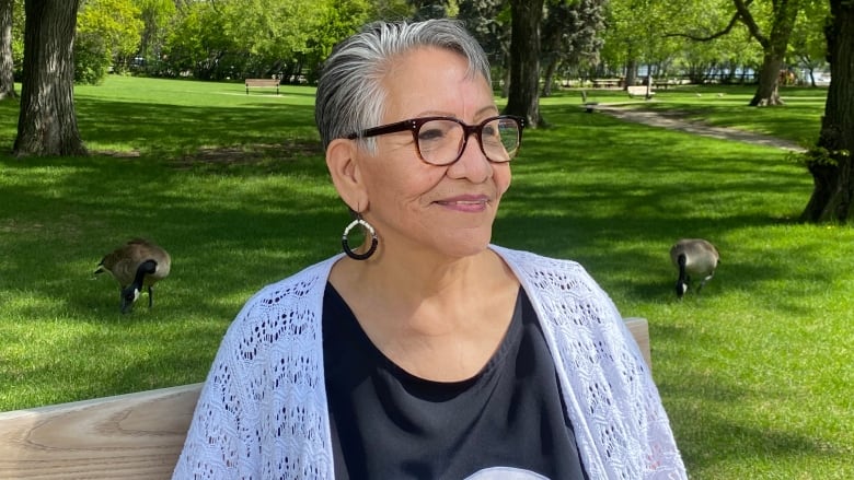 A woman smiles on a park bench. 