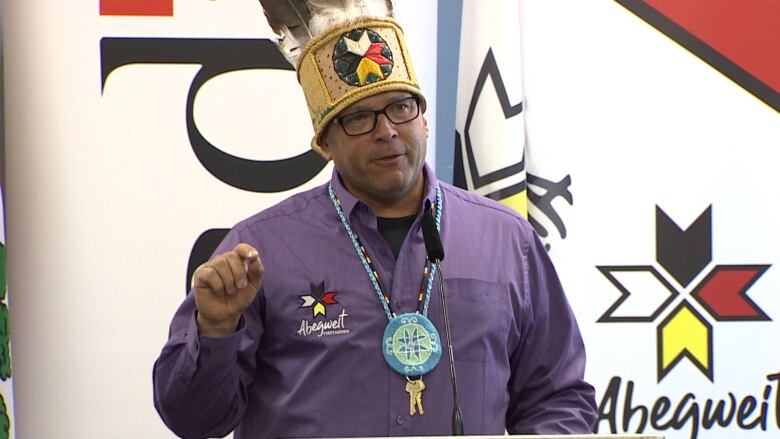 A man wearing an indigenous headdress with feathers stands in front of a podium and gives a speech.  