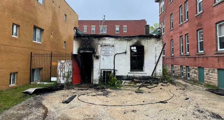 The back of a small convenience store is pictured. The openings of the door and a small window are blackened after a fire.