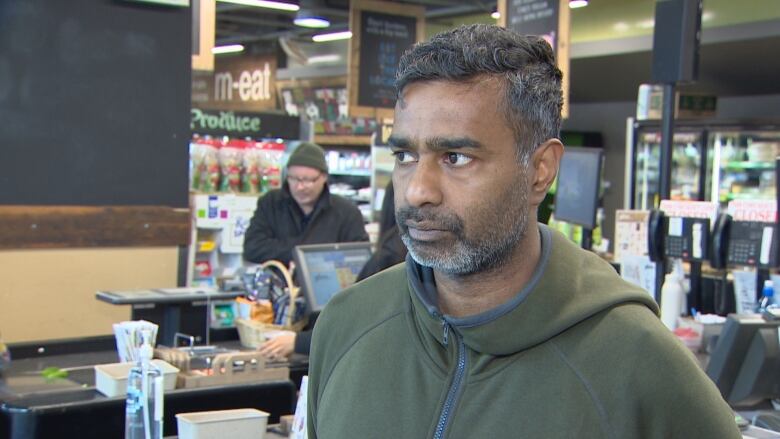 A man in a green sweater in a grocery store looks out the window.