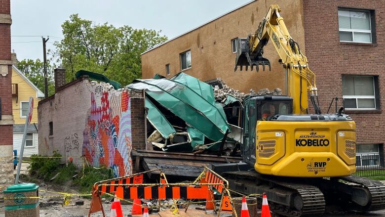 A yellow excavator demolishes a building.