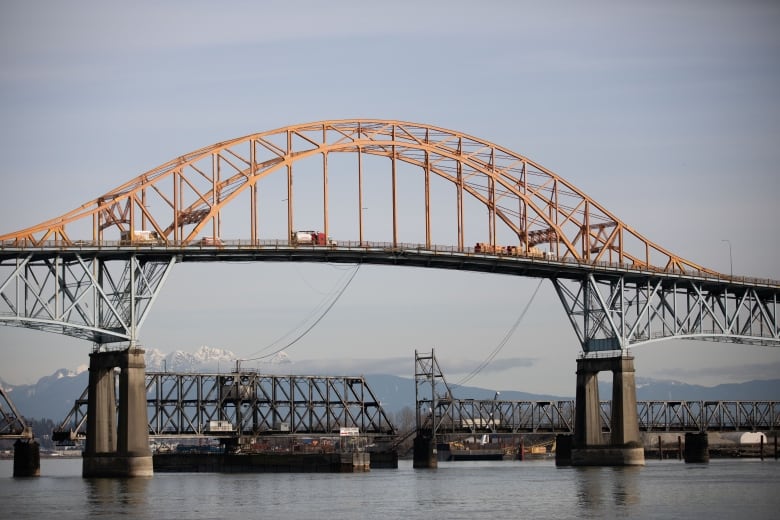 A large bridge with yellow tresses and snow-capped mountains in the background.