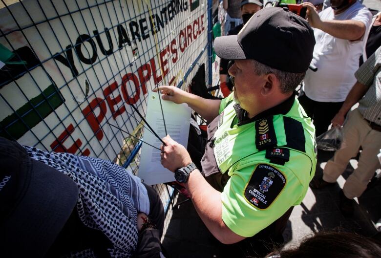 A university staff person, escorted by campus security, puts up trespass notices on a pro-Palestinian encampment at the University of Toronto on May 24, 2024.