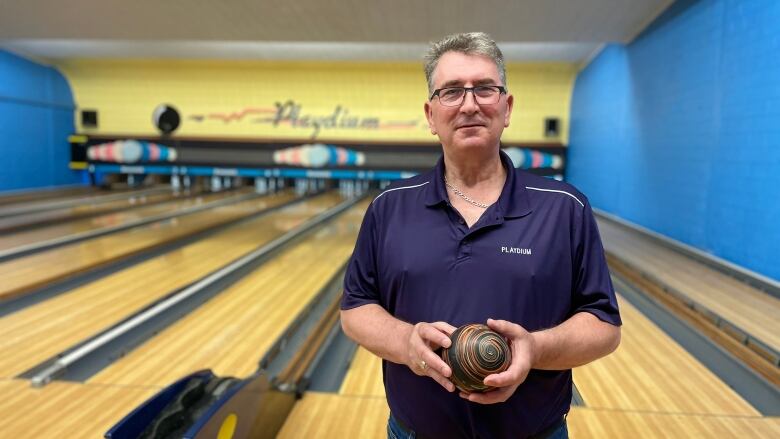 A man holds a five-pin bowling ball in front of bowling lanes.