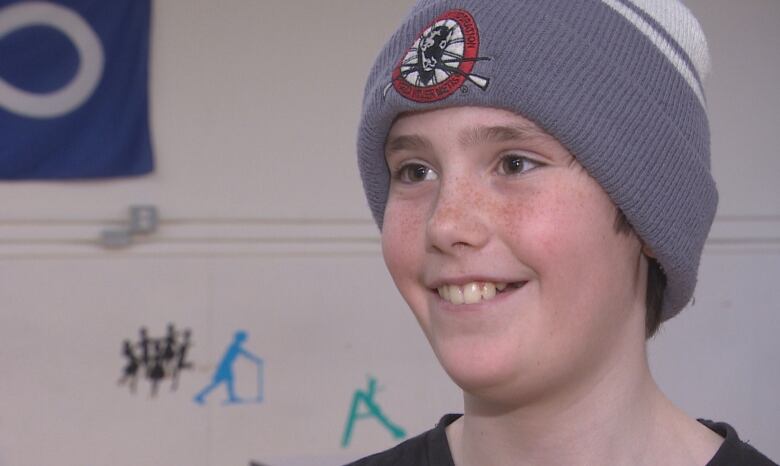 A 13 year old boy grins, wearing a Manitoba Mtis Federation toque he won playing bingo.