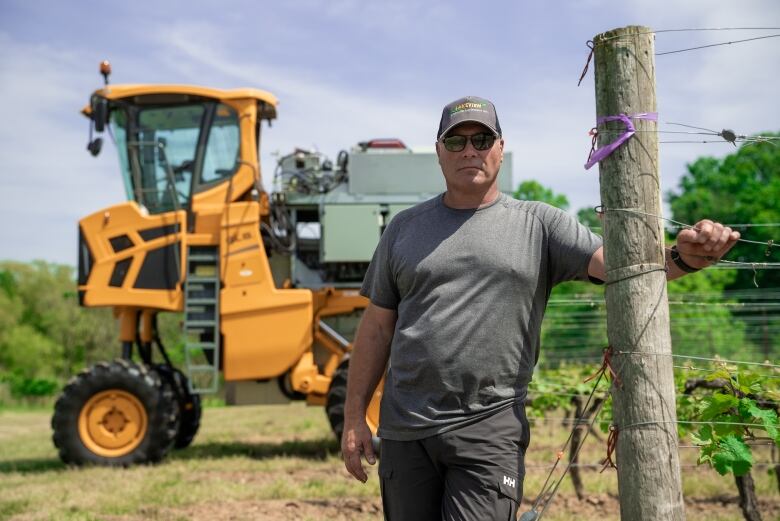 A man wearing a grey T-shirt and ball cap stands in front of a modified harvester that helps control fungus through UV light and hydrogen peroxide.