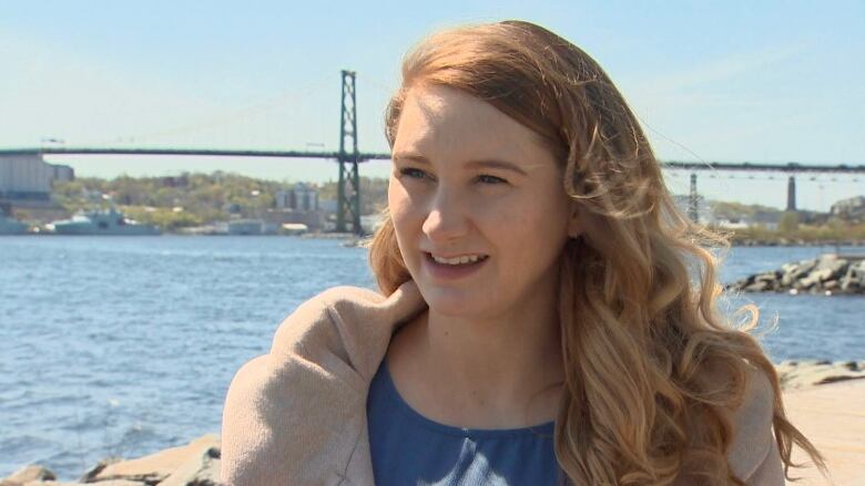 A woman stands by a harbour with a bridge in the background.