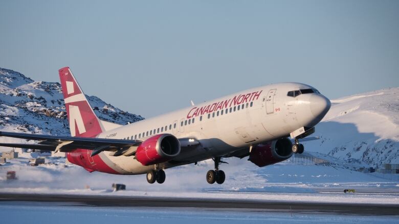 A Boeing jet with white and red livery takes off from a snowy Northern airport on a cloudless, sunny day.