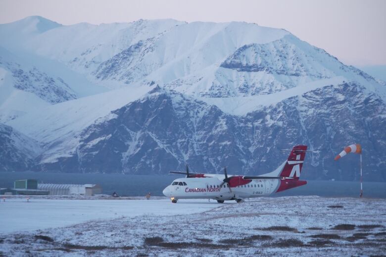 A twin-propeller plane is pictured taxiing. In the background is the vast snowy mountain range of Bylot Island.