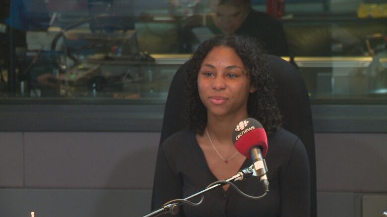 A woman smiles in front of a microphone in a radio studio.