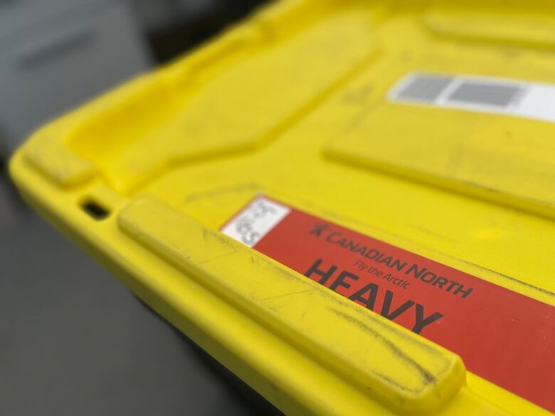 A red sticker on a yellow cover of a large plastic tote bin, warning the bin is heavy at 75 pounds.