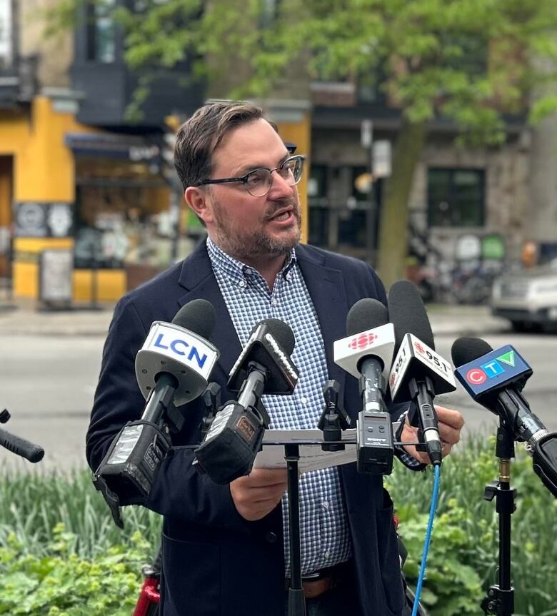 A man speaks into microphones while standing outside