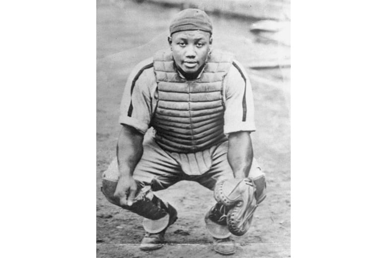 A dark-complected, clean shaven baseball catcher is shown in a black and white photograph that appears to be decades old.